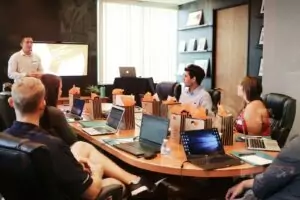Un formateur donnant une session de formation à un groupe de professionnels autour d'une table dans une salle de réunion, avec des ordinateurs portables et des blocs-notes.