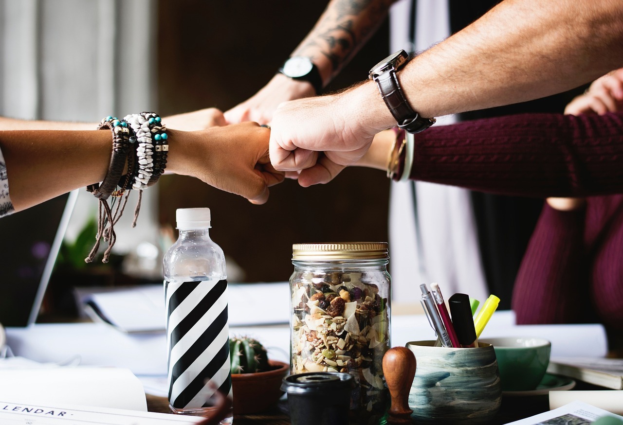 Quatre collègues joignant leurs mains au centre, symbolisant l'accord et la collaboration après la résolution d'un conflit.