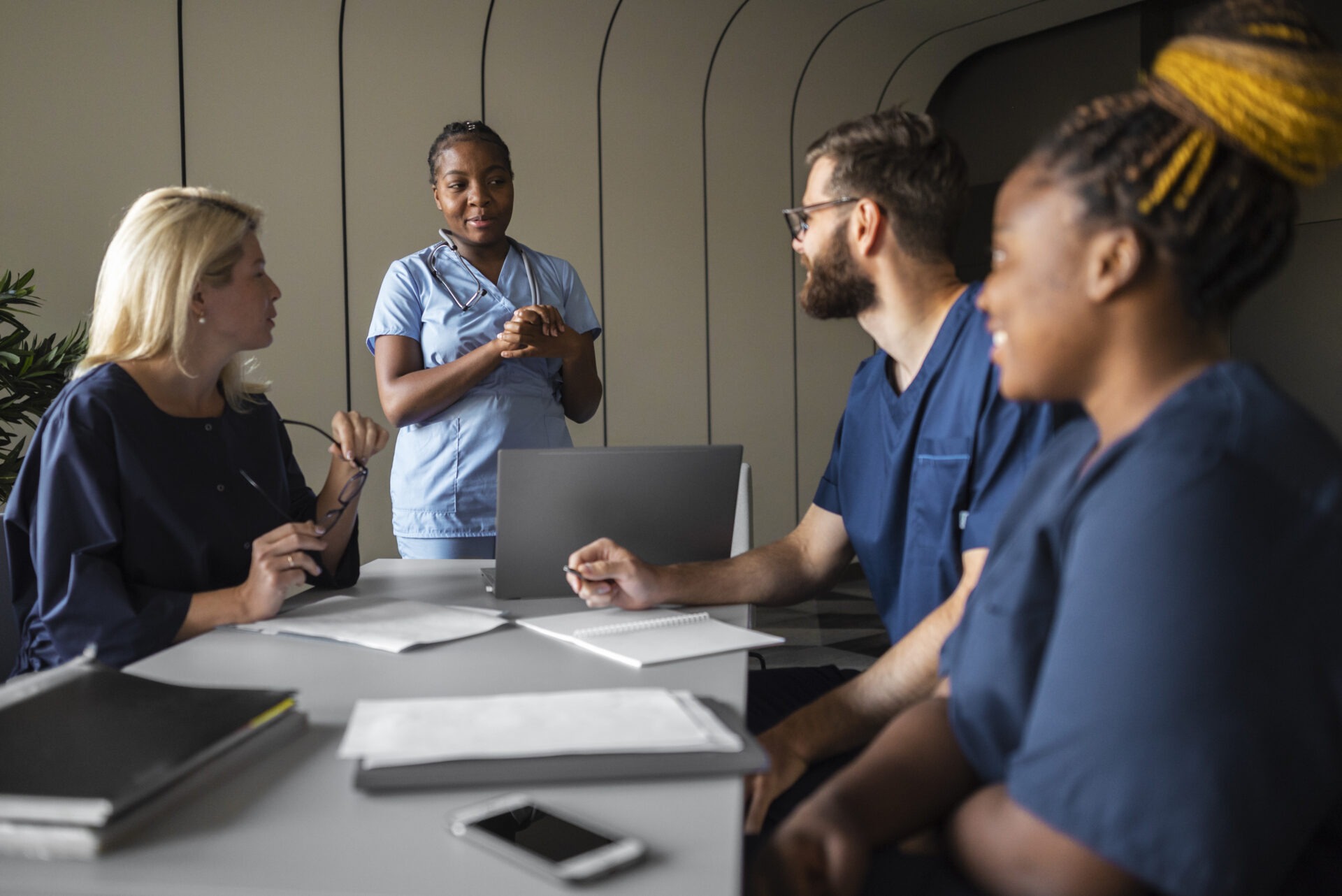 Un groupe de six personnes assises autour d’une table de réunion équipée d’ordinateurs portables et de cahiers dans une salle au design moderne.