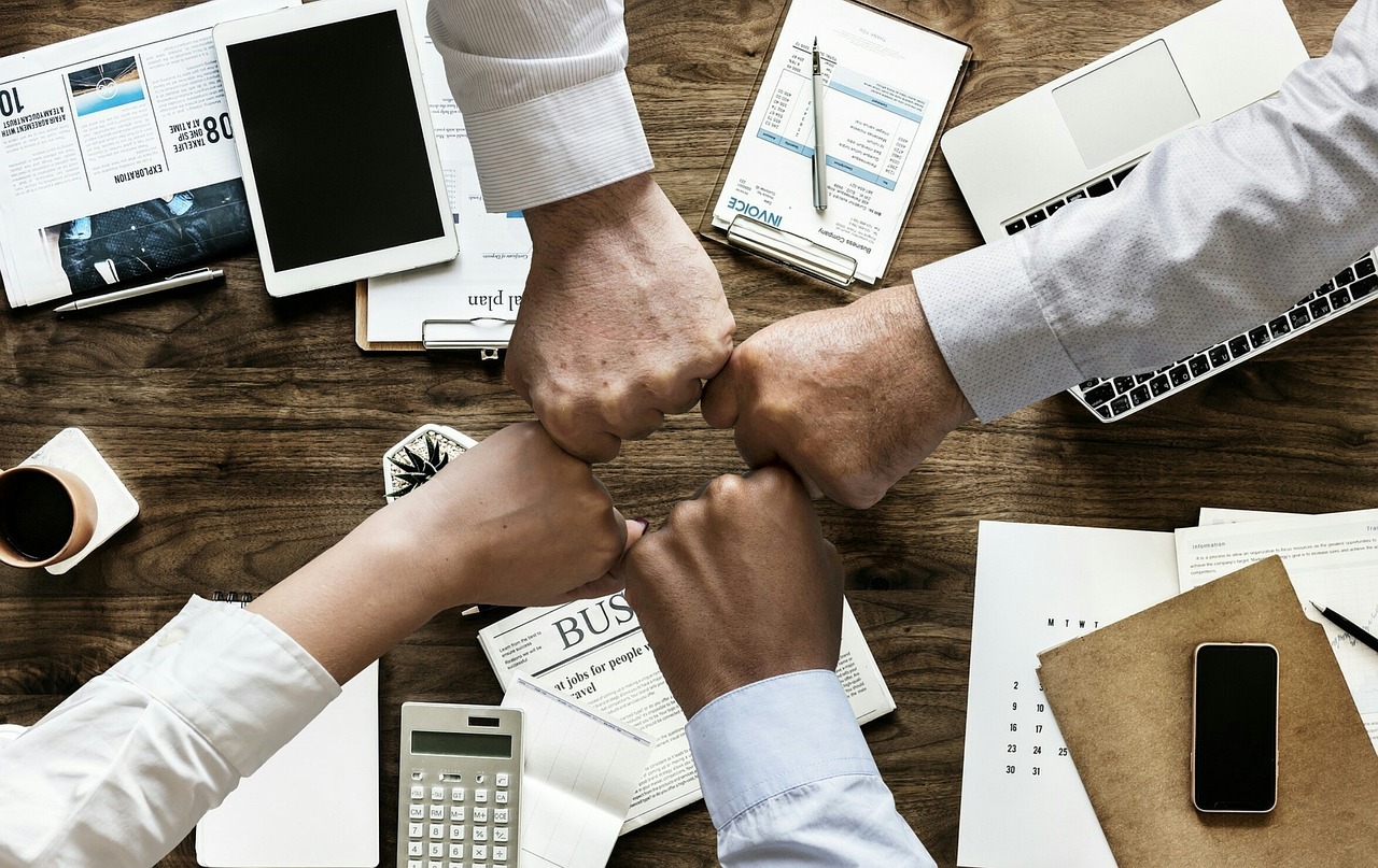 La Confiance : Un actif précieux pour l’entreprise Quatre personnes se tapant le poing au-dessus d’une table en bois avec des appareils électroniques et des documents.