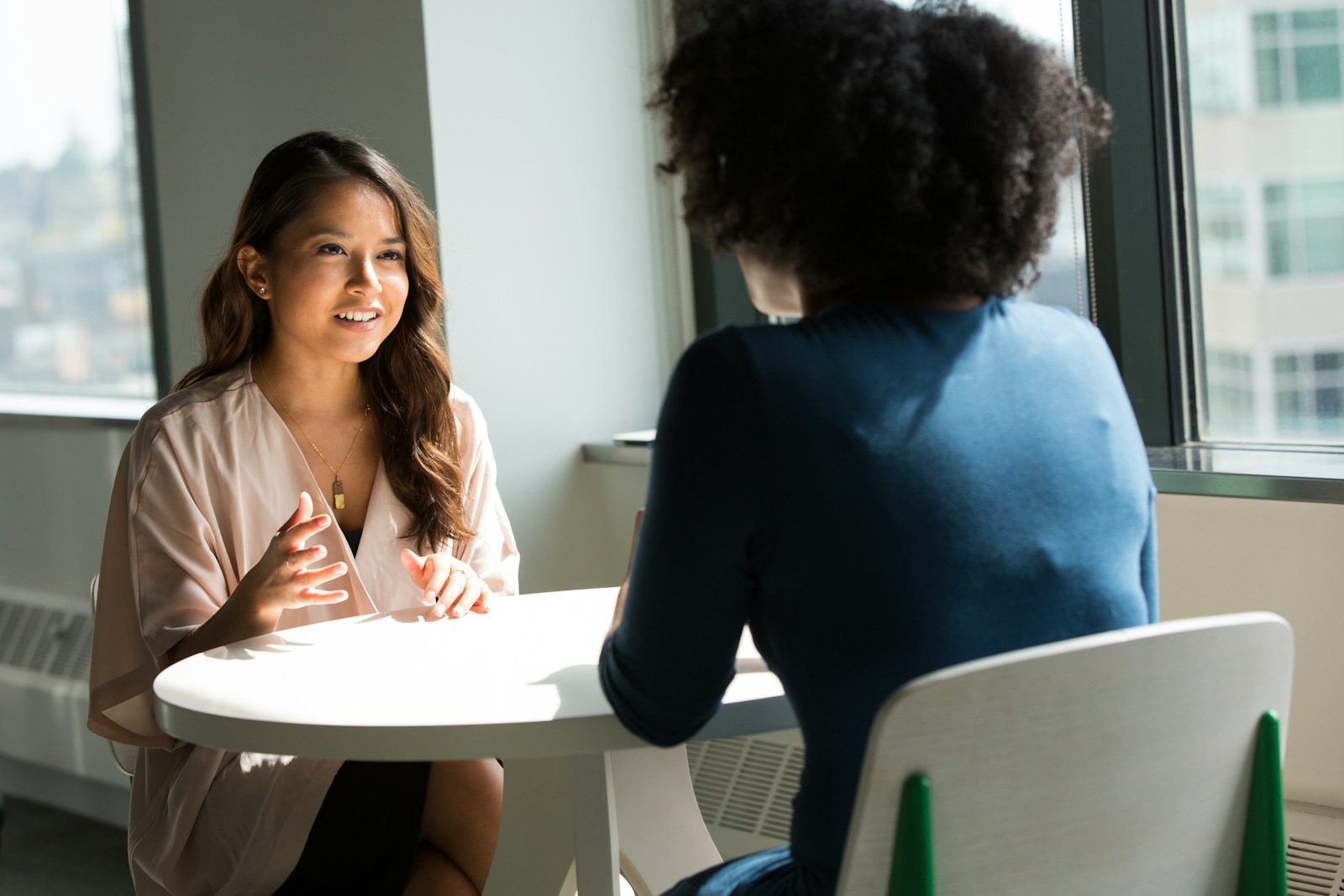 Désamorcer le conflit au travail :Deux femmes discutent autour d'une table dans un bureau lumineux, illustrant une communication bienveillante et active.