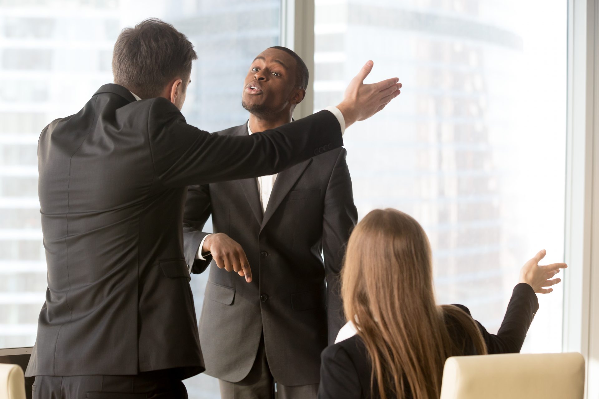 Formation gestion des conflits en entreprise : Trois collègues en costume en désaccord animé lors d’une réunion professionnelle dans un bureau moderne