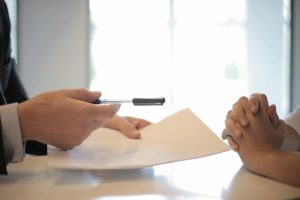 Formation professionnelle entreprise 2025 : deux personnes échangent des documents lors d’un entretien ou d’une signature, avec un stylo tendu vers l’interlocuteur.